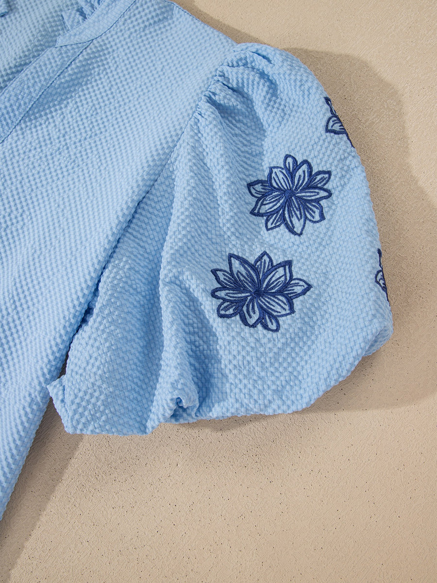 Light blue seersucker blouse with puff sleeves and dark blue floral embroidery.