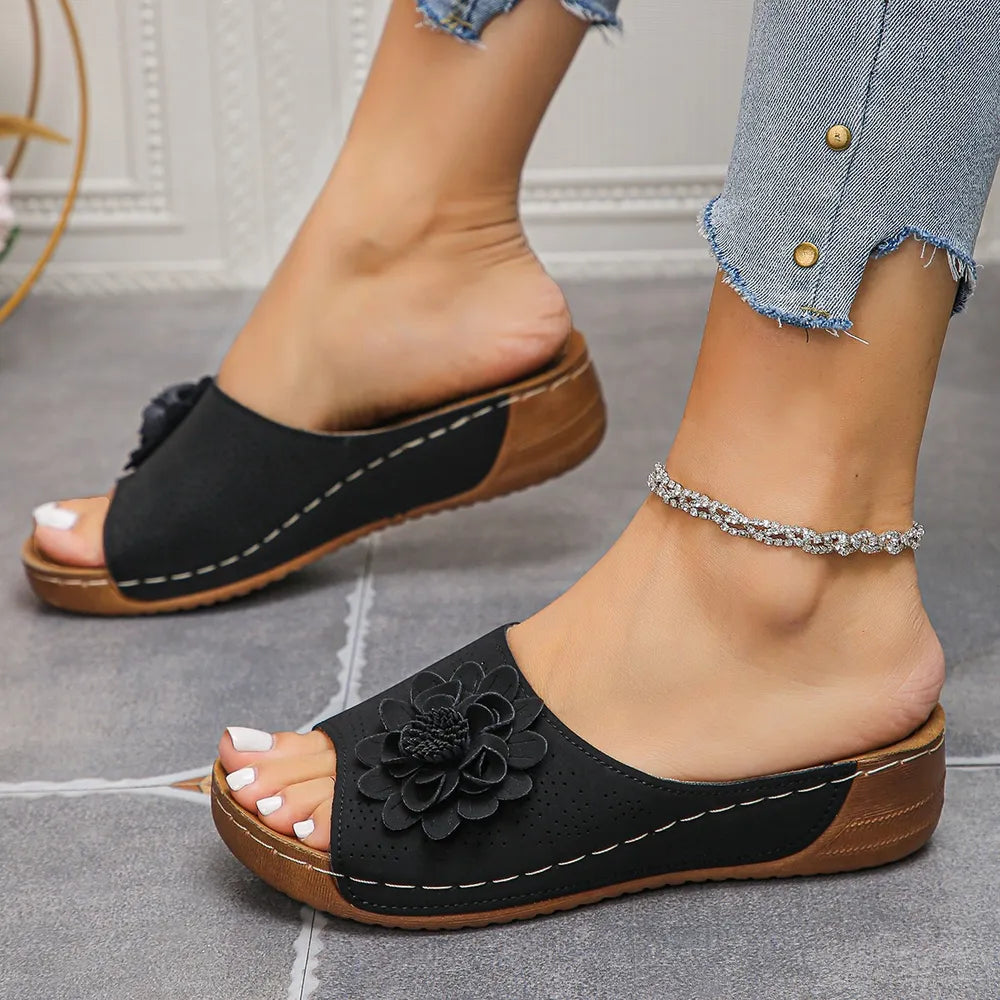 Black perforated floral wedge slides with contrast stitching and wooden sole.