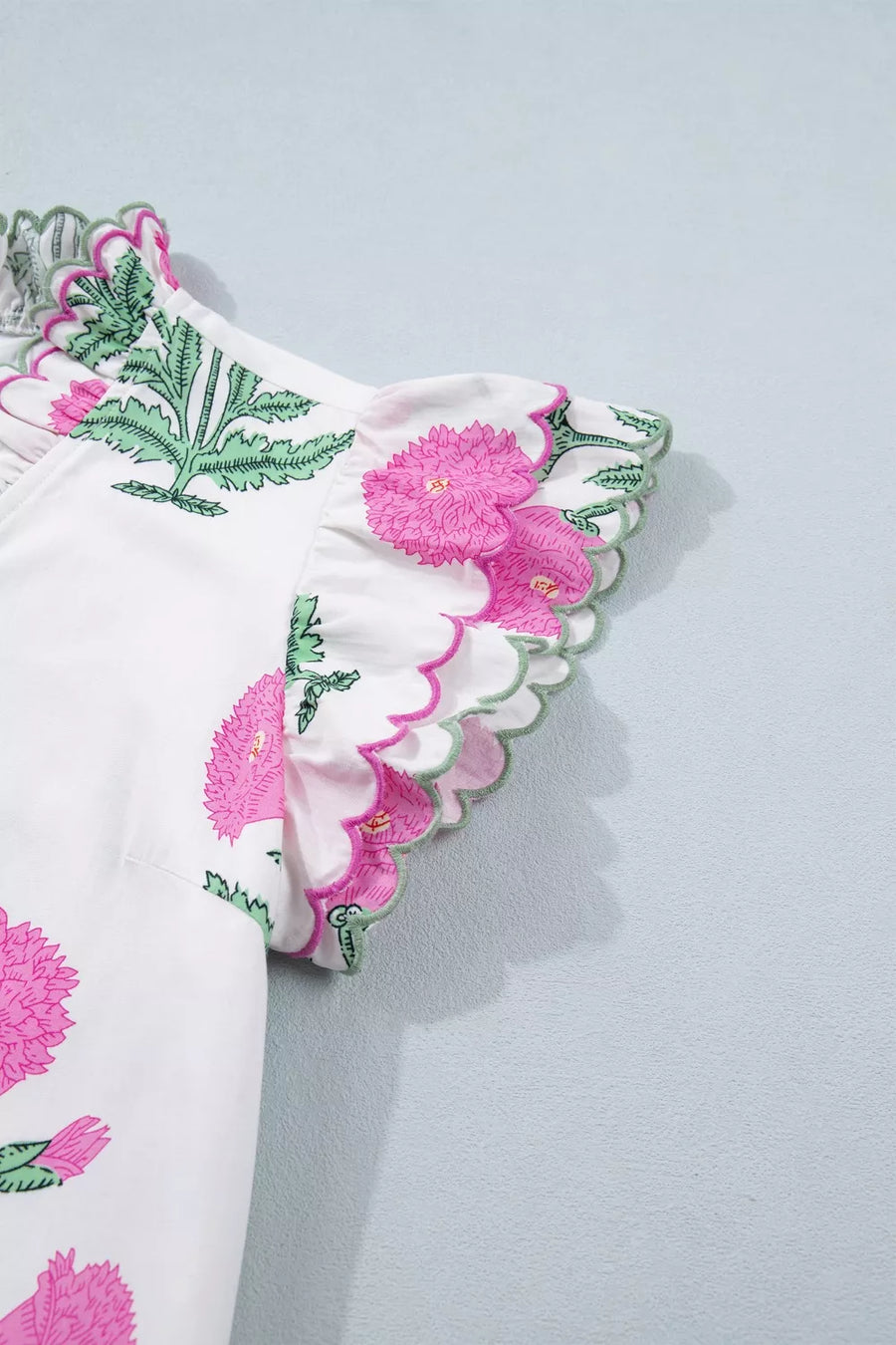 White mini dress with pink floral print, green leaves, and ruffled scalloped trim sleeves.