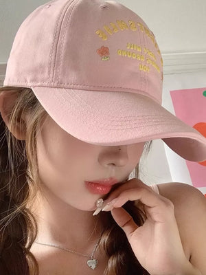 Pink baseball cap with yellow embroidered text and flower detail