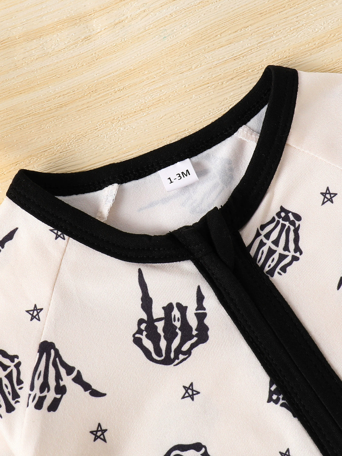 Beige baby one-piece with black skeleton hand print and stars pattern, black trim neckline.