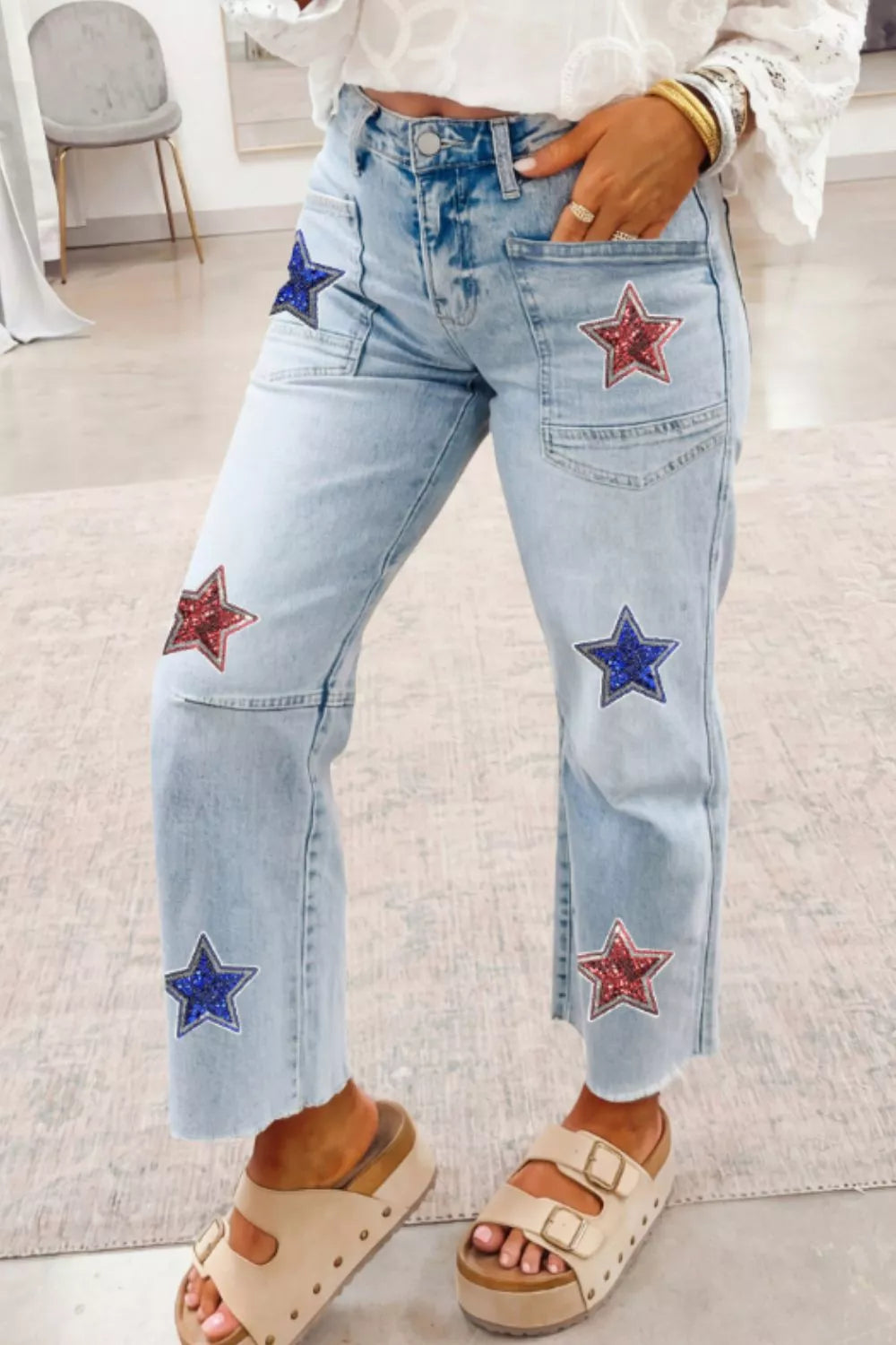 Light wash denim cropped utility jeans with red and blue sequin star patches and frayed hem.