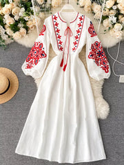 White maxi dress with red and blue embroidery, balloon sleeves, and tassel tie neckline.