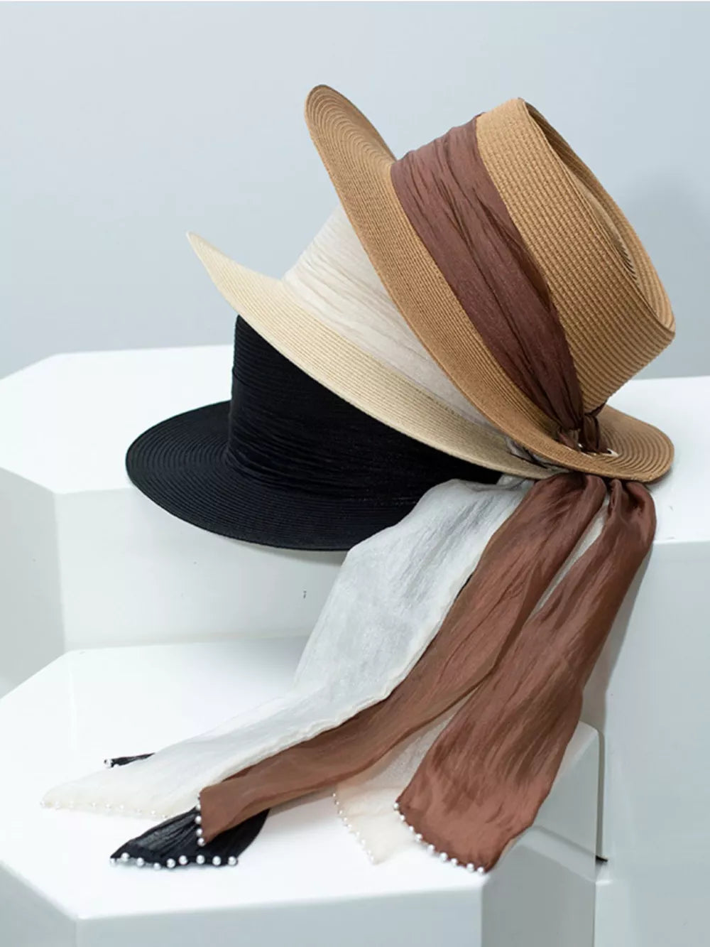 Straw sun hats in brown, ivory, and black with ribbon and pearl embellishments.