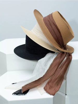 Straw sun hats in brown, ivory, and black with ribbon and pearl embellishments.