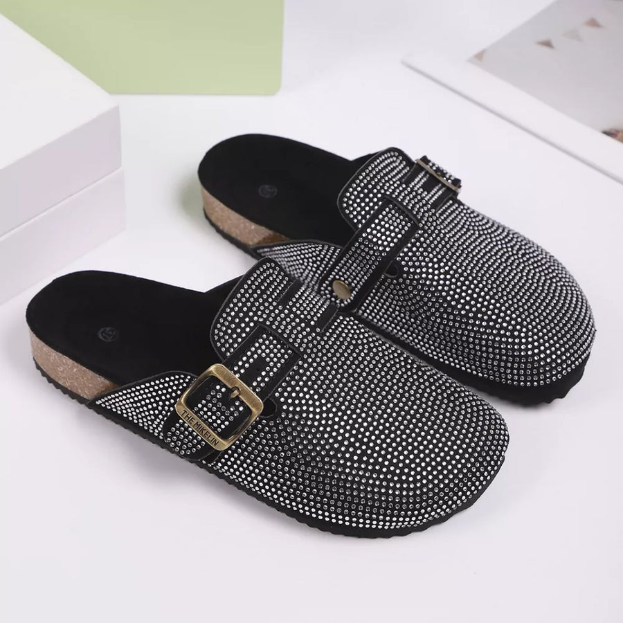 Black rhinestone buckle slip-on mules with cork sole and adjustable strap.