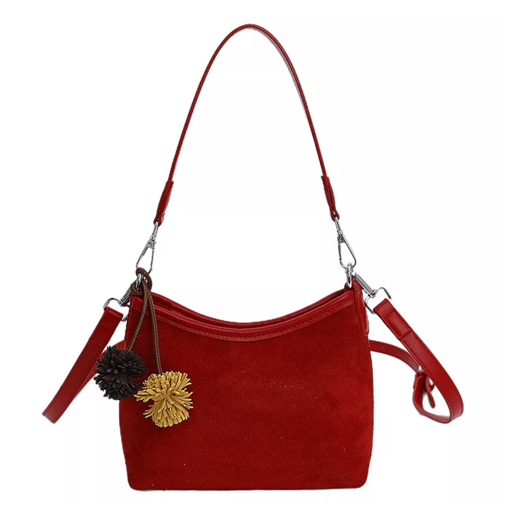 Red suede crossbody bag with two fluffy pom-pom charms and adjustable strap.