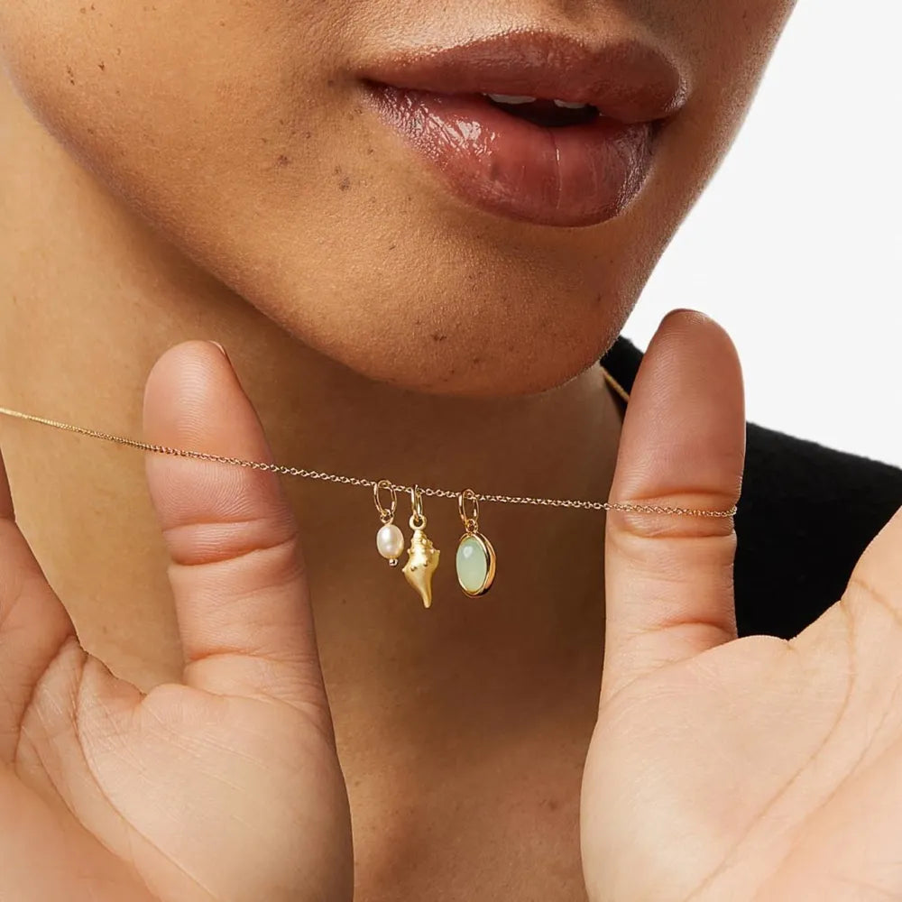 Gold necklace with pearl, conch shell, and gemstone charms.