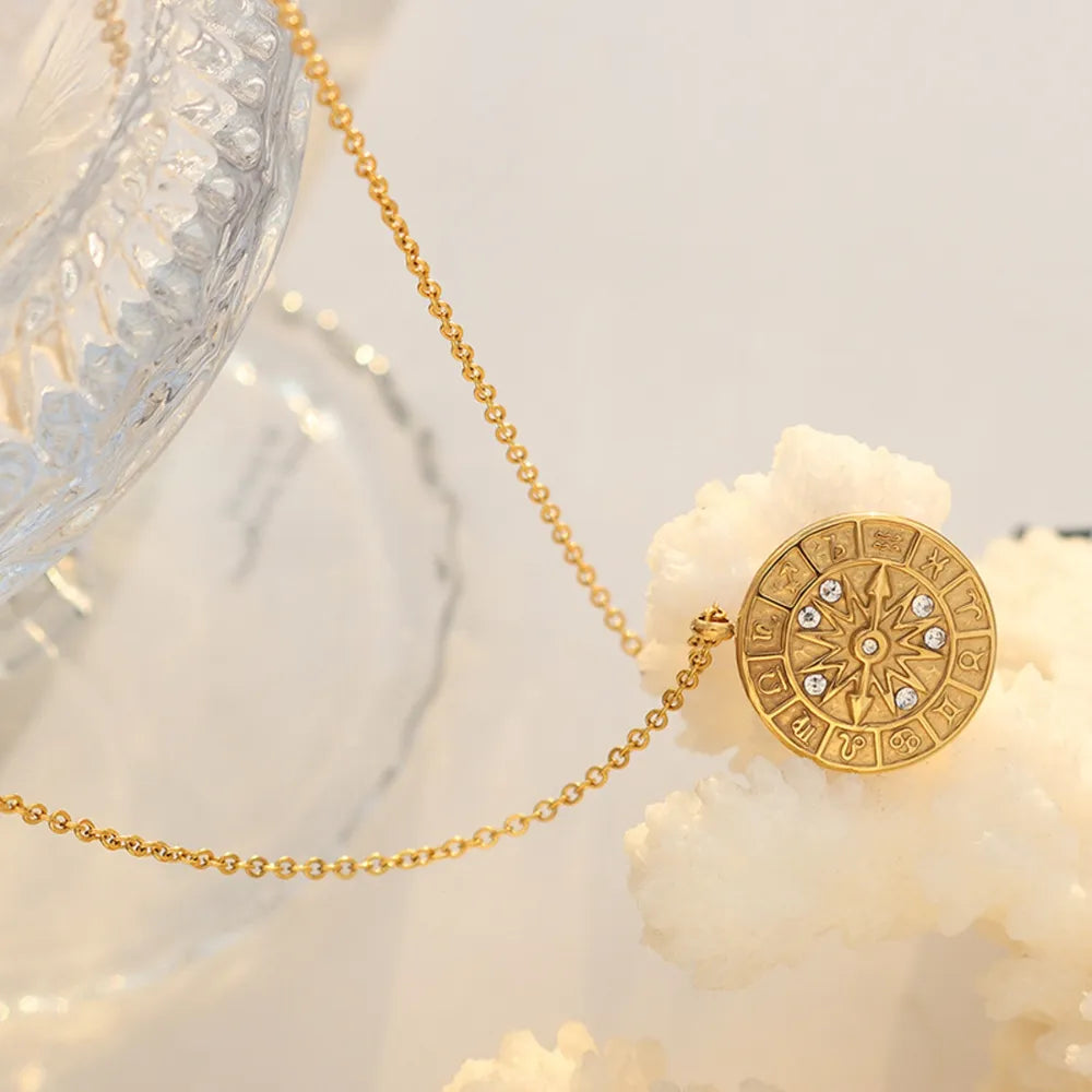 Gold zodiac compass pendant necklace with celestial details and clear stones.