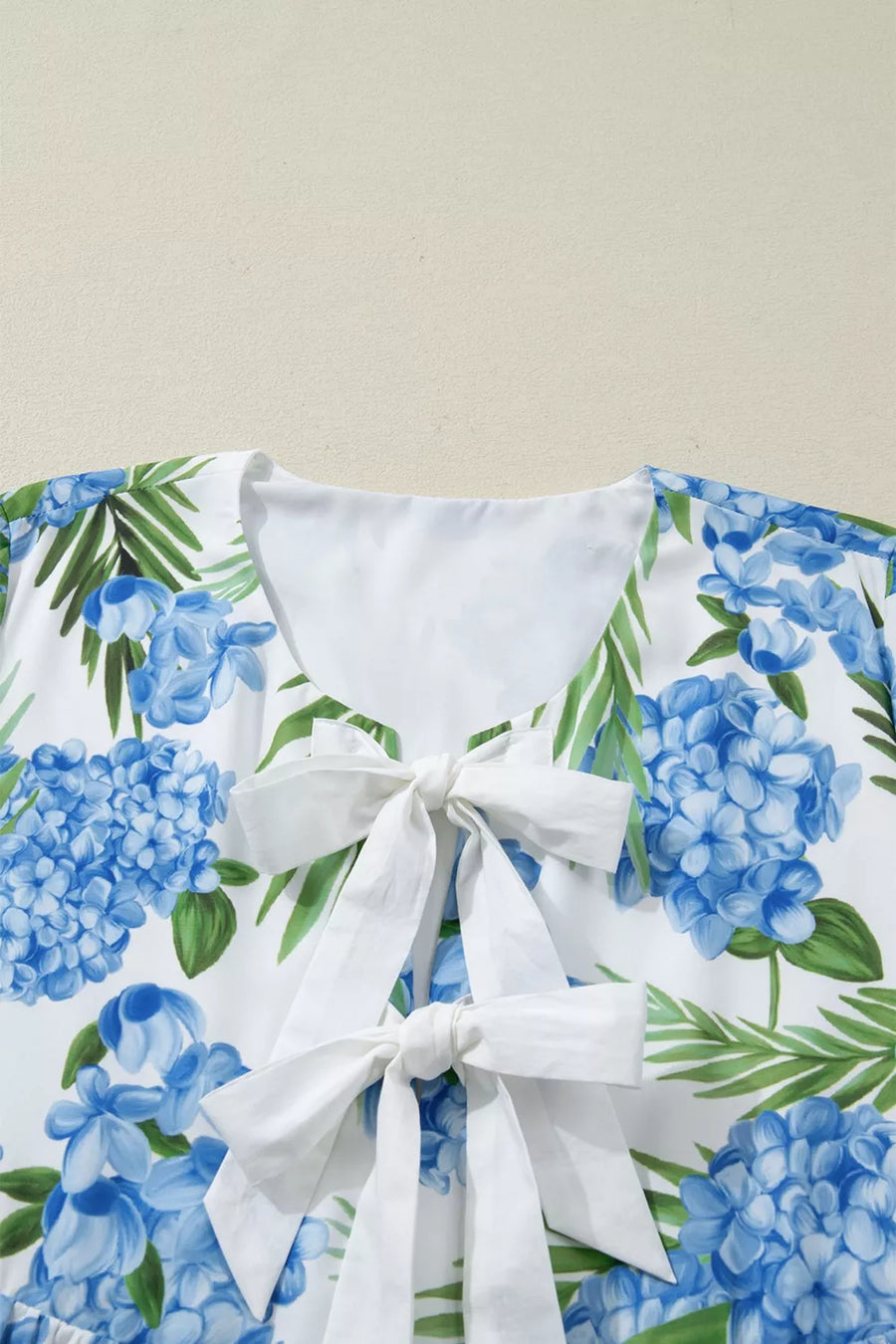 Ruffled mini dress with hydrangea and palm print, featuring a white neckline with two bow details.