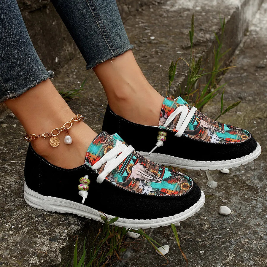 Black canvas slip-on flats with colorful embroidered bull head pattern and rope detail.