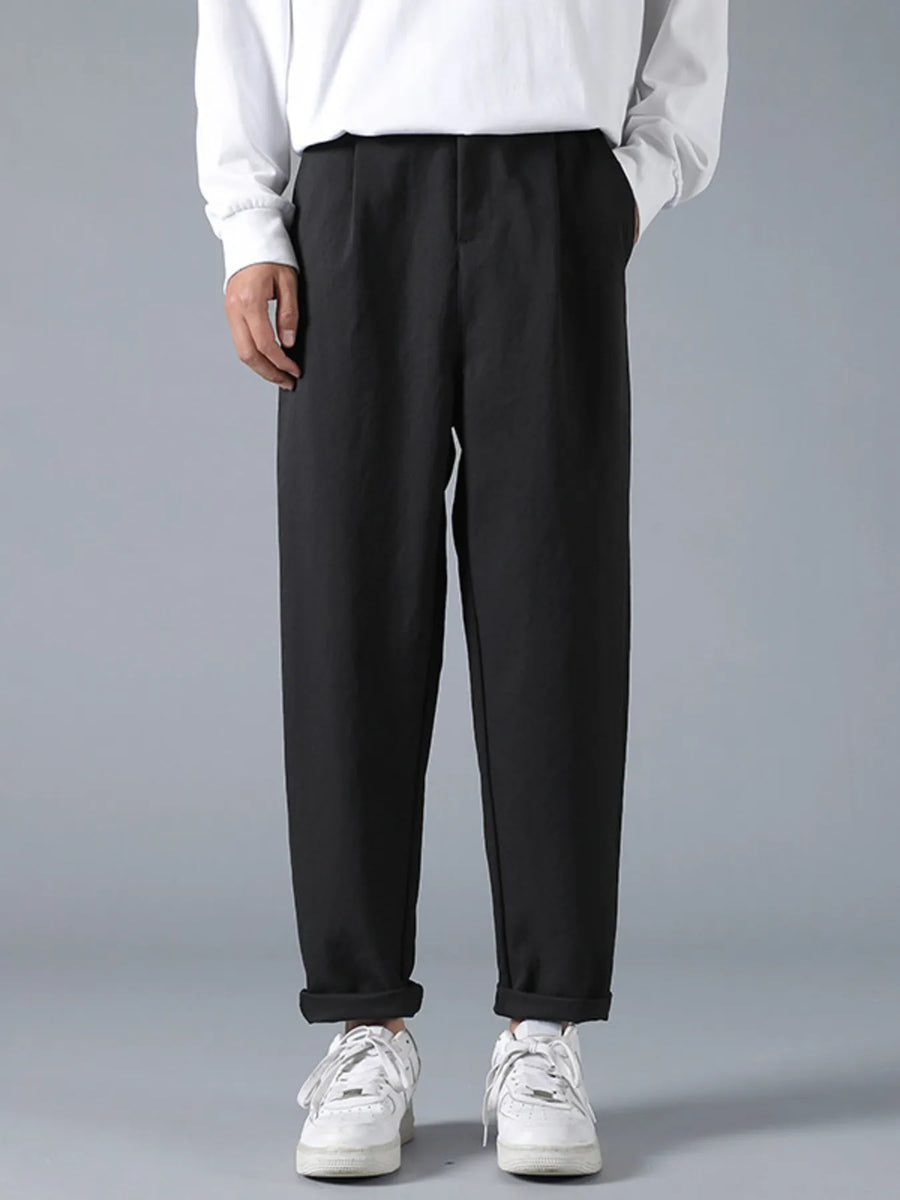 Black casual loose fit pleated trousers with cuffed hems, worn with white sneakers.