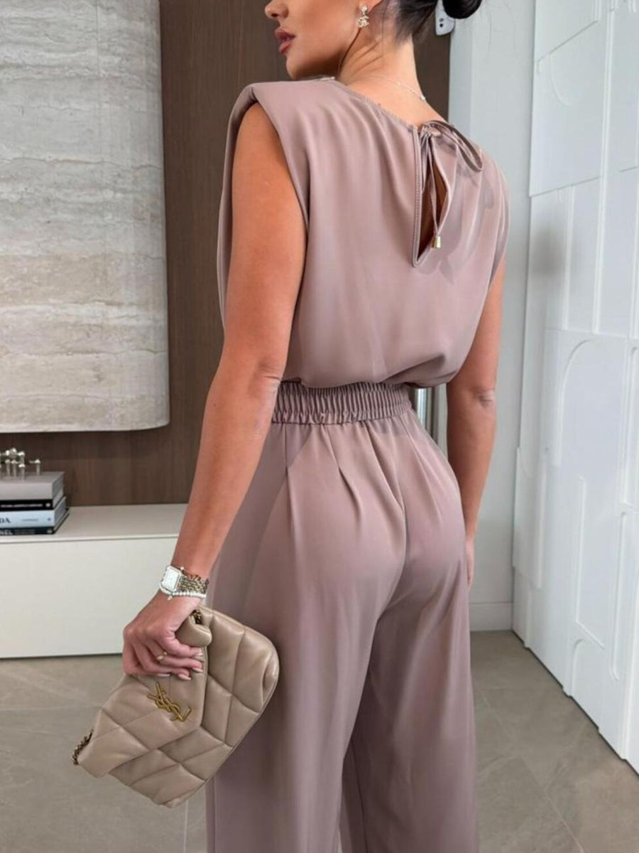 Mocha wide-leg jumpsuit with padded shoulders and tie-back detail.
