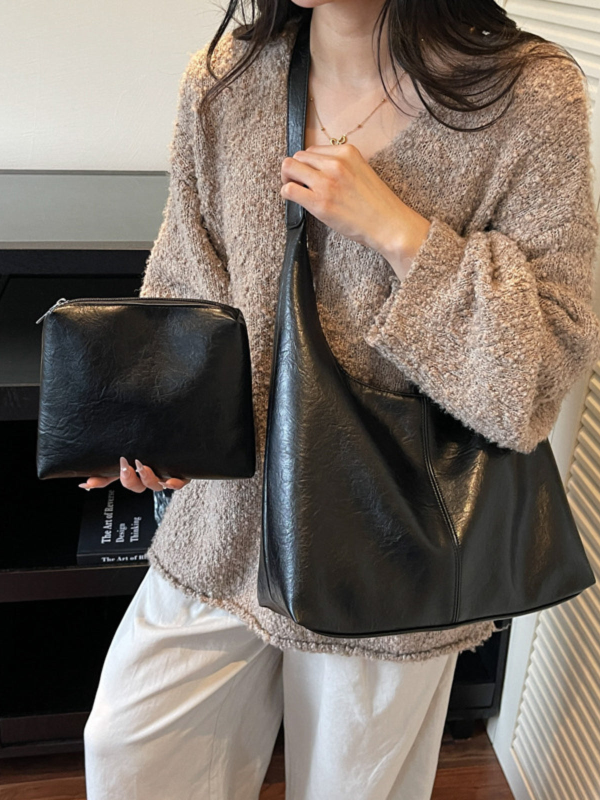 Black faux leather shoulder bag and matching pouch displayed by a woman wearing a textured sweater.
