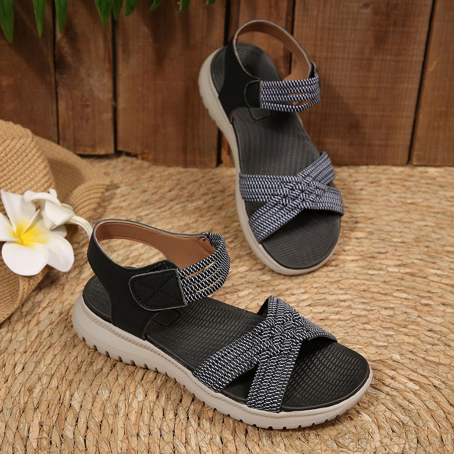 Black woven strap open-toe flat sandals with adjustable ankle strap and knot detail.