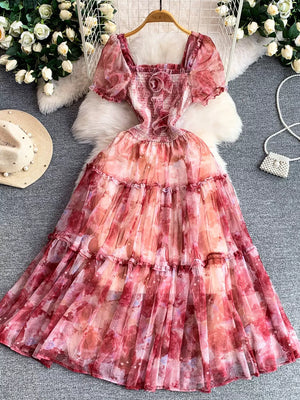 Floral tiered midi dress with smocked bodice, puff sleeves, and square neckline in a watercolor pink and red print.