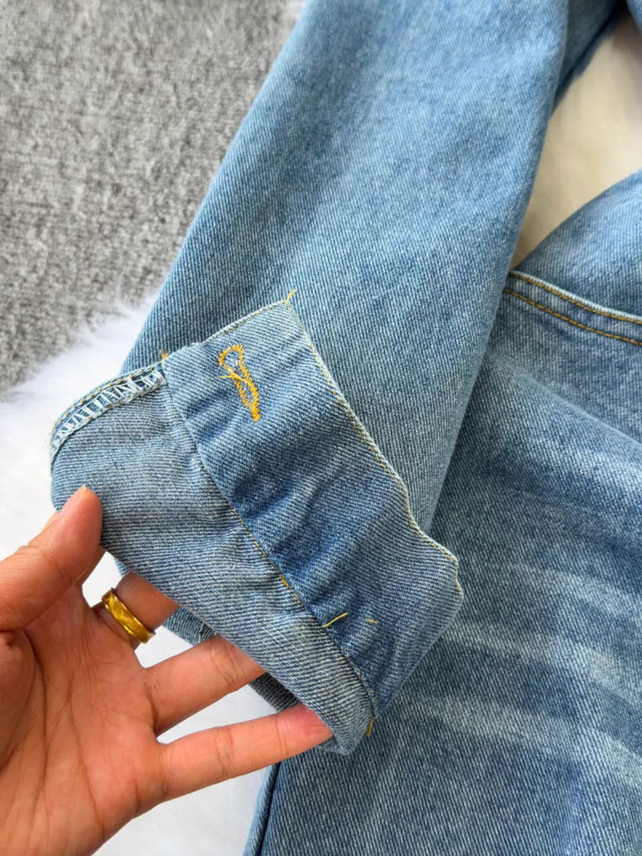 Denim jumpsuit sleeve cuff with yellow embroidery detail and visible stitching.