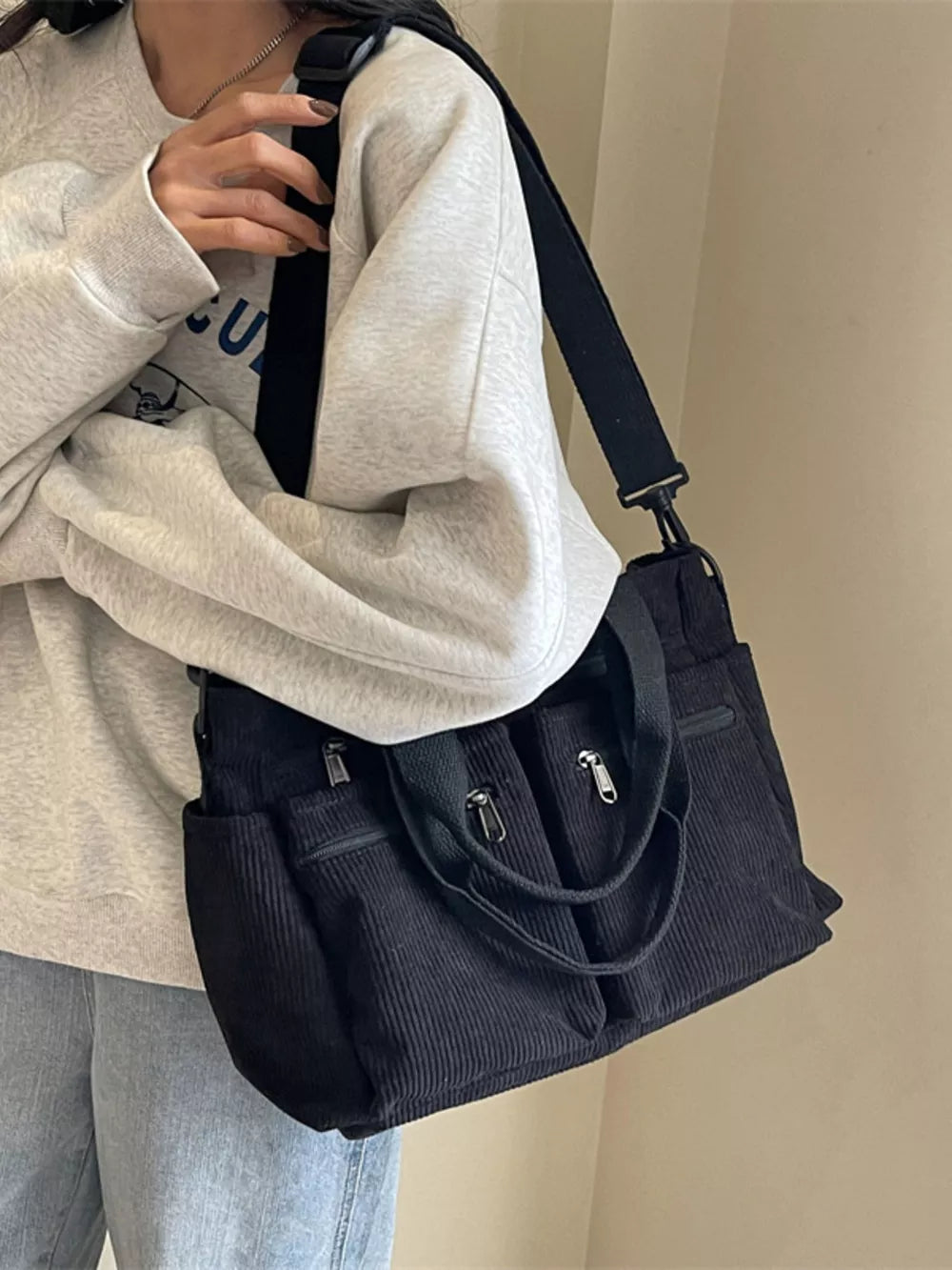 Black corduroy crossbody bag with multiple zip pockets and adjustable strap