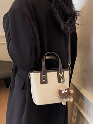 Mini leather crossbody bag in beige with brown trim and a fuzzy charm.