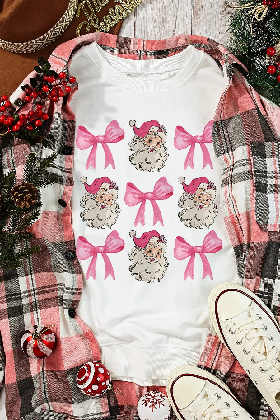 White crewneck sweatshirt with a repeating pattern of Santa faces and pink bows.