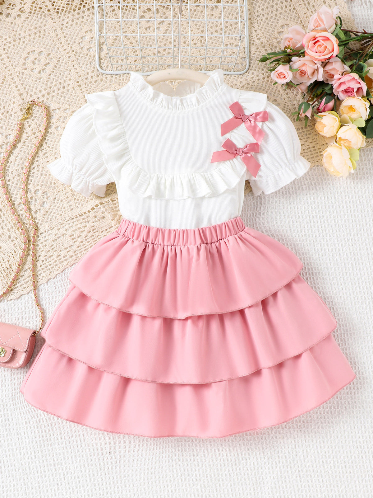 Toddler white ruffled top with pink bows and pink tiered skirt with elastic waistband.