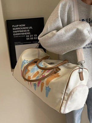 Vibrant canvas duffle bag in off white with colorful star design and brown leather handles.
