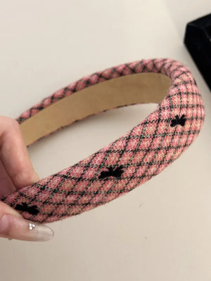 Pink tweed headband with black bow details and a diamond pattern.