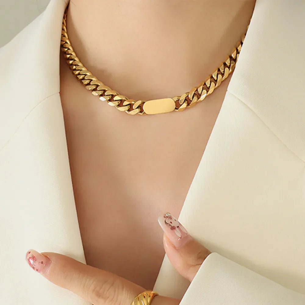 Gold Cuban link necklace with a flat oval accent, worn with a white blazer.