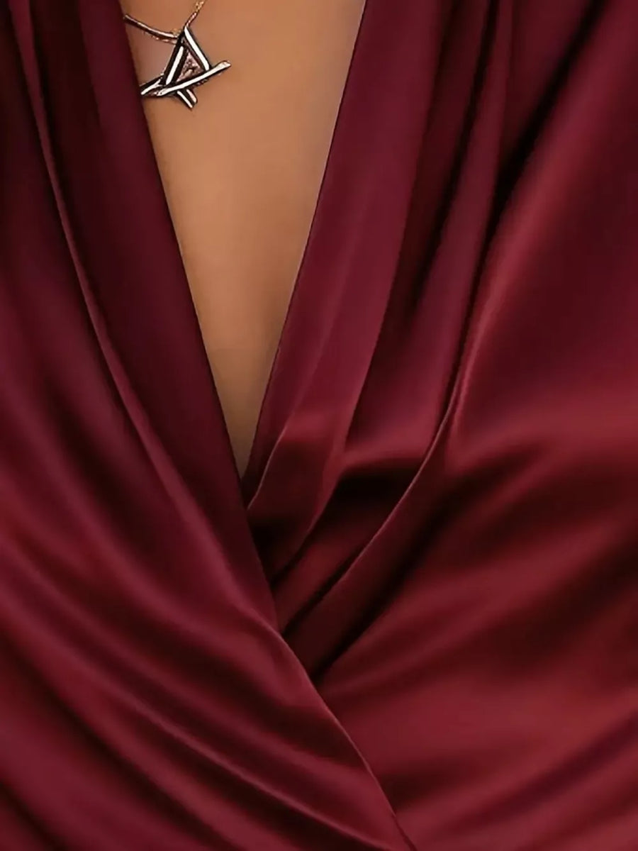 Wine red satin surplice blouse with draped neckline and geometric pendant necklace.
