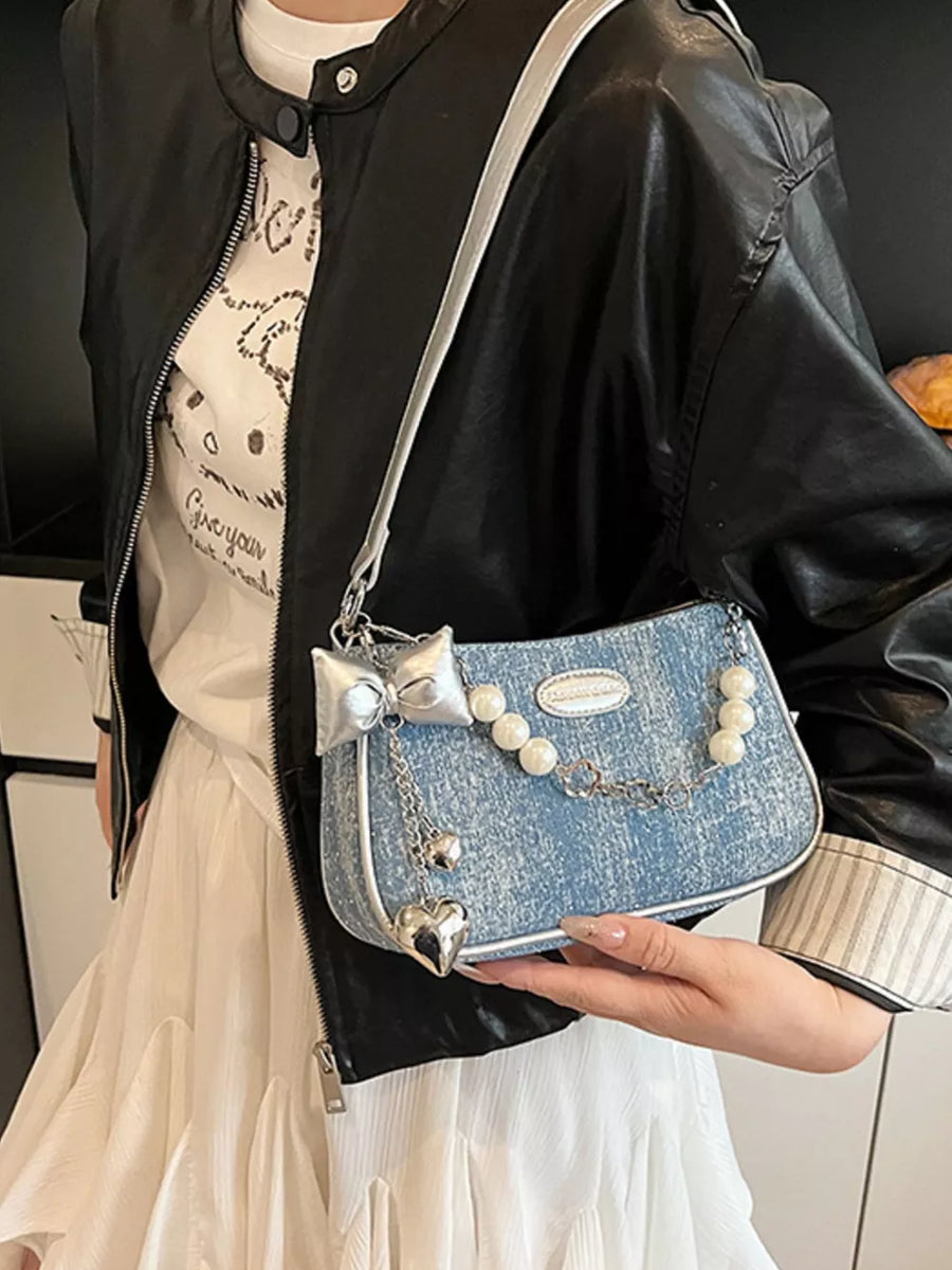 Light denim shoulder bag with pearl chain, bow, and heart charms.