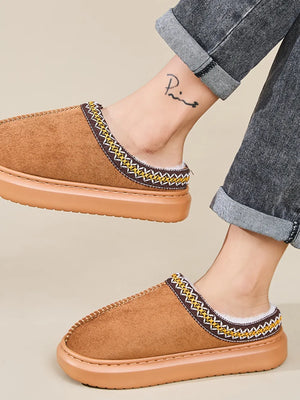 Caramel shearling house slippers with embroidered trim and white lining.