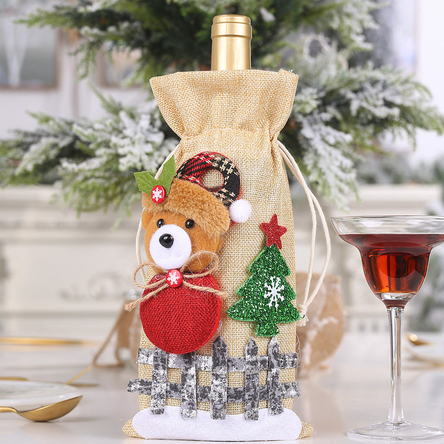 Festive wine bottle gift bag with a plush bear, red ball, and Christmas tree detail.