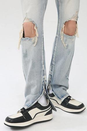 Light wash denim trousers with distressed knee slits and zippered ankles.