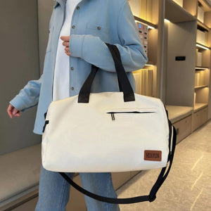 Creamy-white nylon duffel bag with black straps and adjustable shoulder strap, featuring a zippered pocket and logo patch.