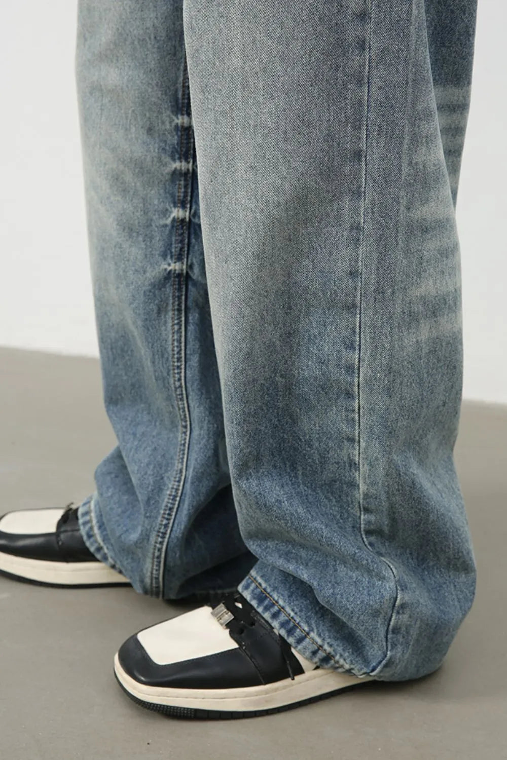 Baggy wash denim trousers in medium blue with a relaxed fit, styled with black and white sneakers.