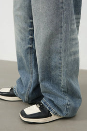 Baggy wash denim trousers in medium blue with a relaxed fit, styled with black and white sneakers.