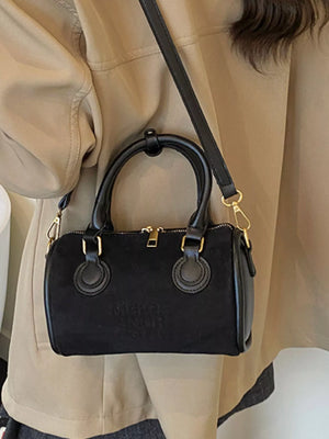 Small black barrel crossbody bag with top handles and gold hardware.