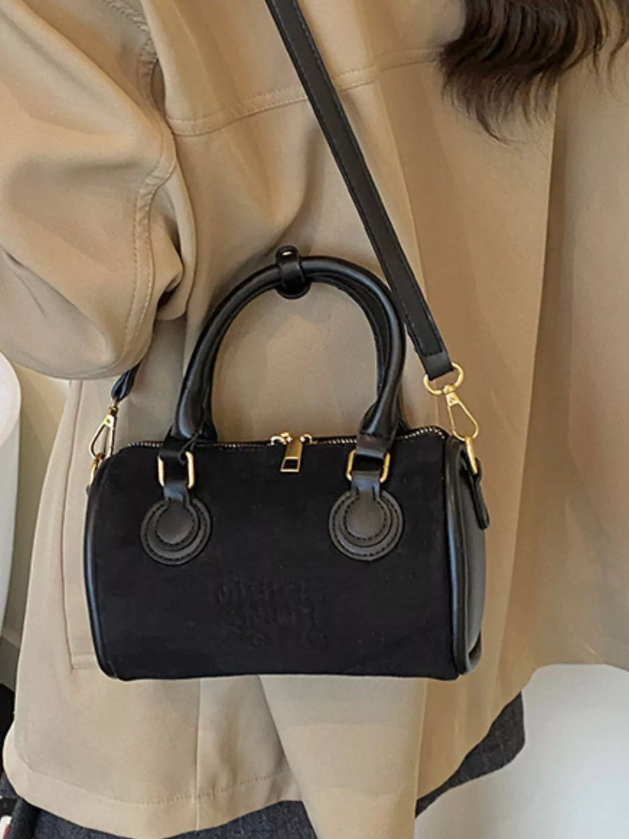 Small black barrel crossbody bag with top handles and gold hardware.