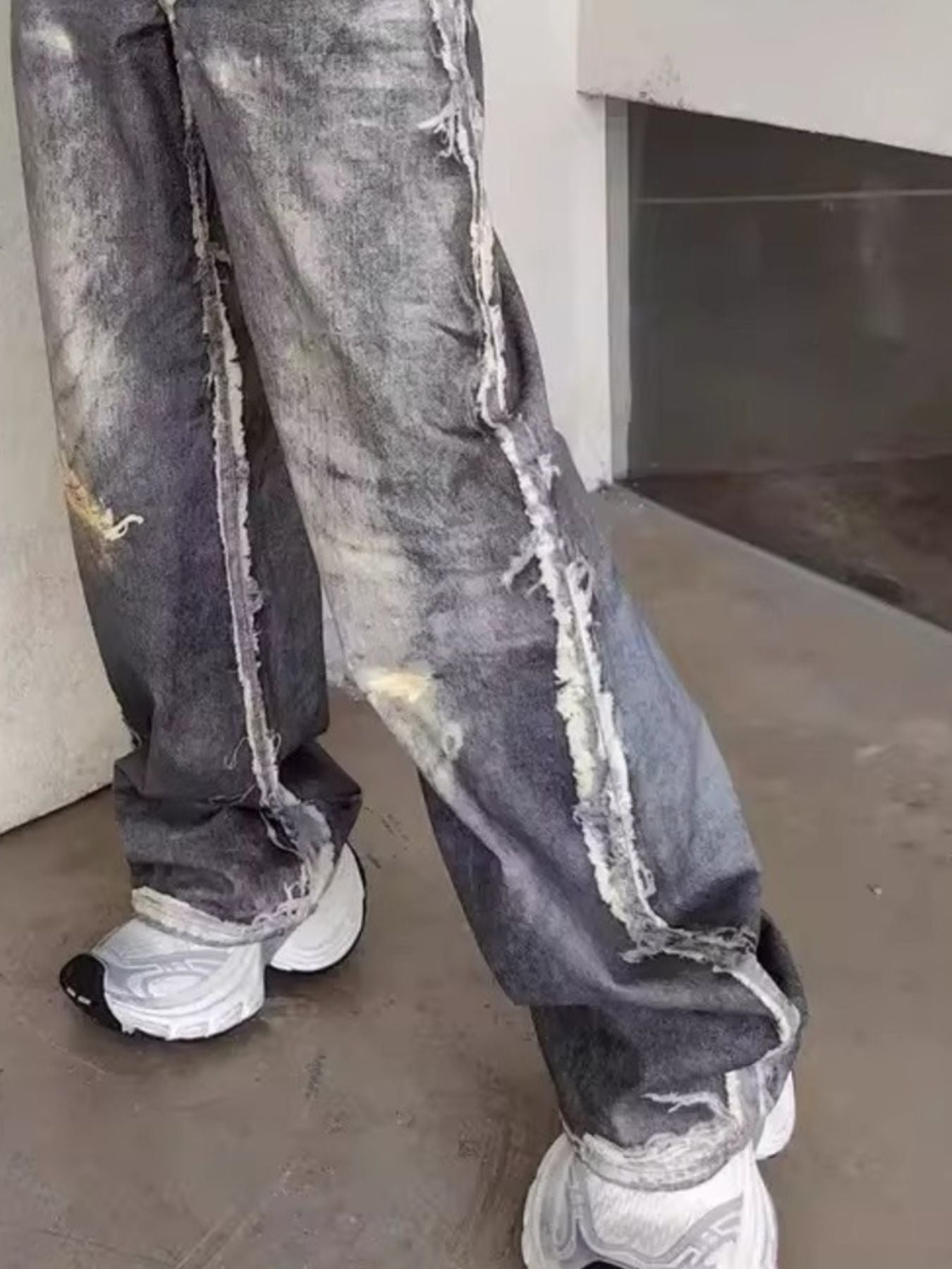 Men's wide-leg jeans in grey denim with heavy distressing and frayed seams.