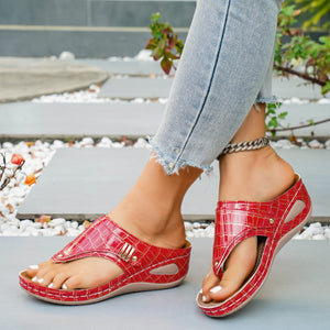 Red crocodile-embossed wedge sandals with thong strap and gold buckle detail.