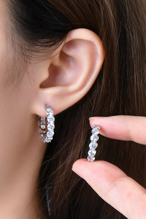 Silver moissanite pavé hoop earrings with sparkling stones, one earring shown on ear, the other held by fingers.