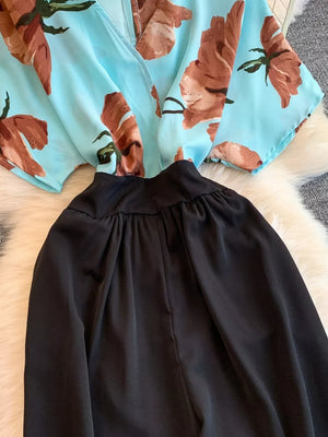 Blue abstract floral print wide-leg romper with black ruched waist and pockets.