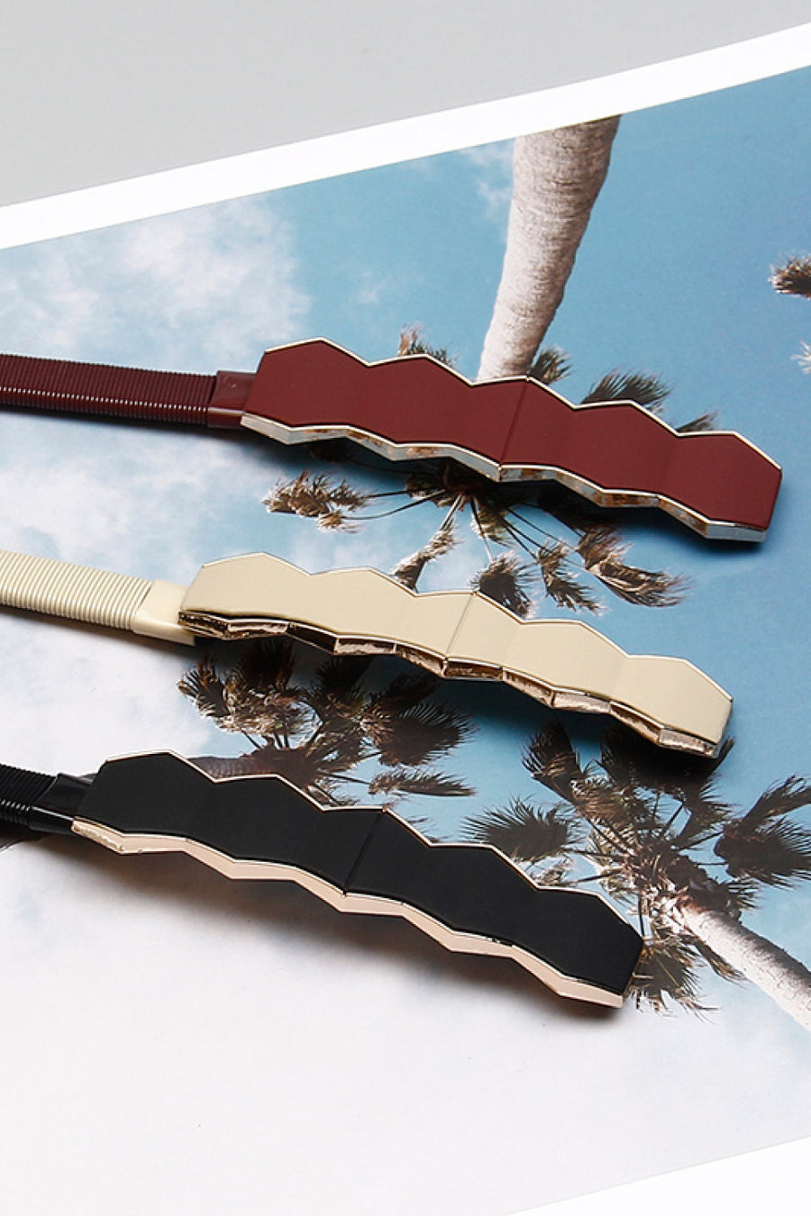 Geometric buckle waist belts in black, cream, and wine with gold trim.