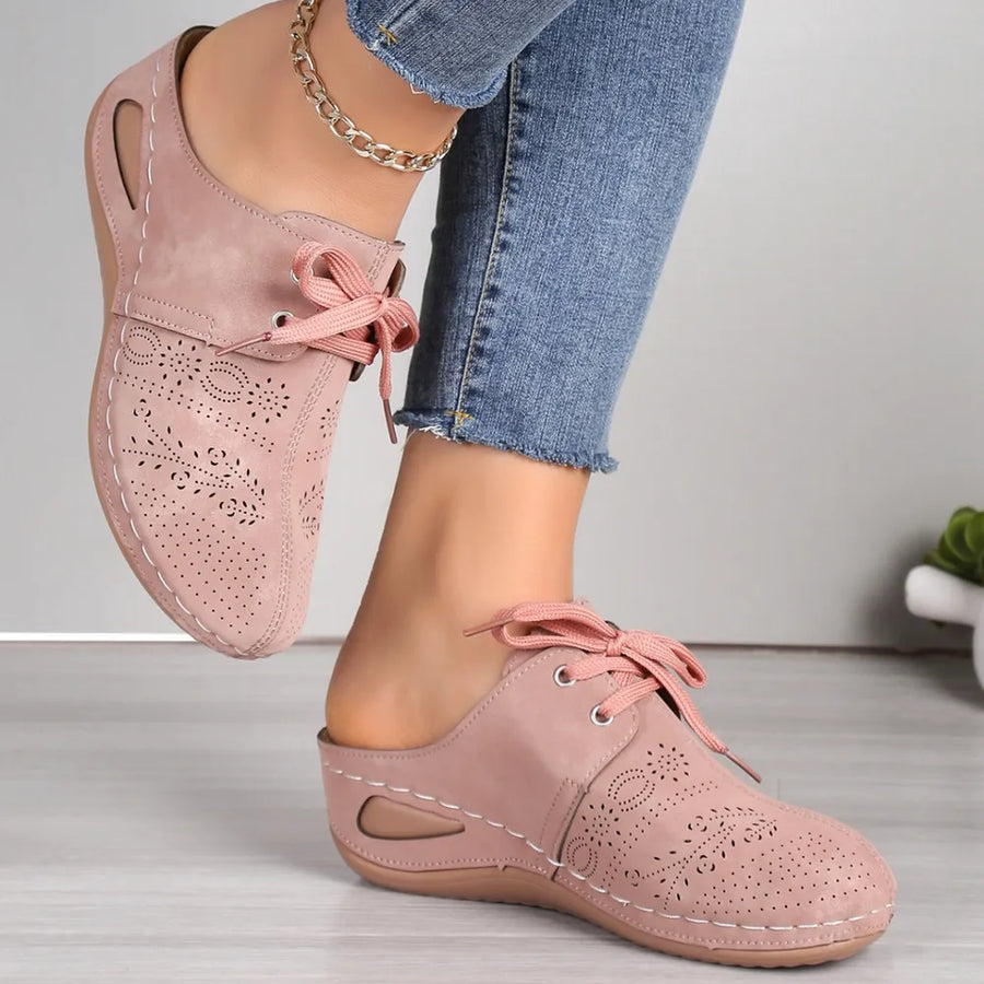 Dusty pink perforated lace-up mule flats with white stitching and a cutout heel.