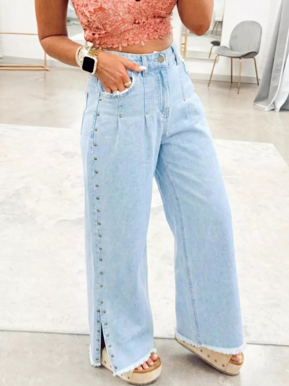 Light wash denim wide-leg jeans with studded side slits and frayed hems.
