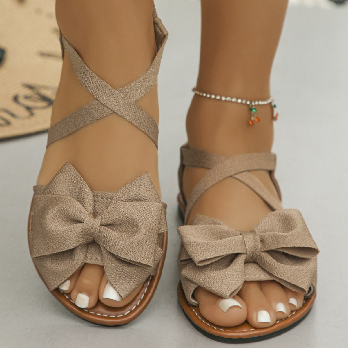 Khaki crisscross bow sandals with ankle straps and a flat sole.