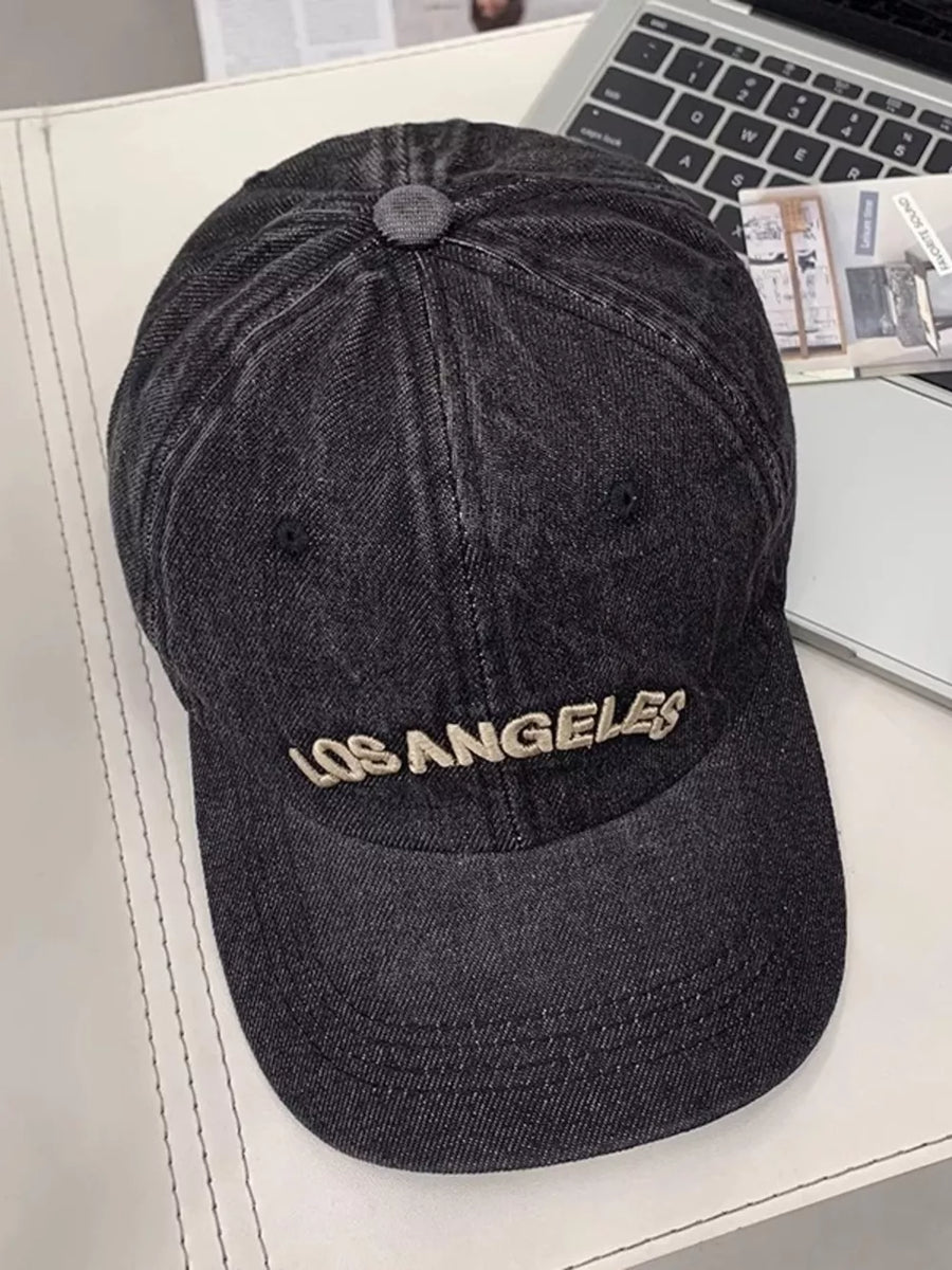 Black denim baseball cap with embroidered Los Angeles text, adjustable strap.