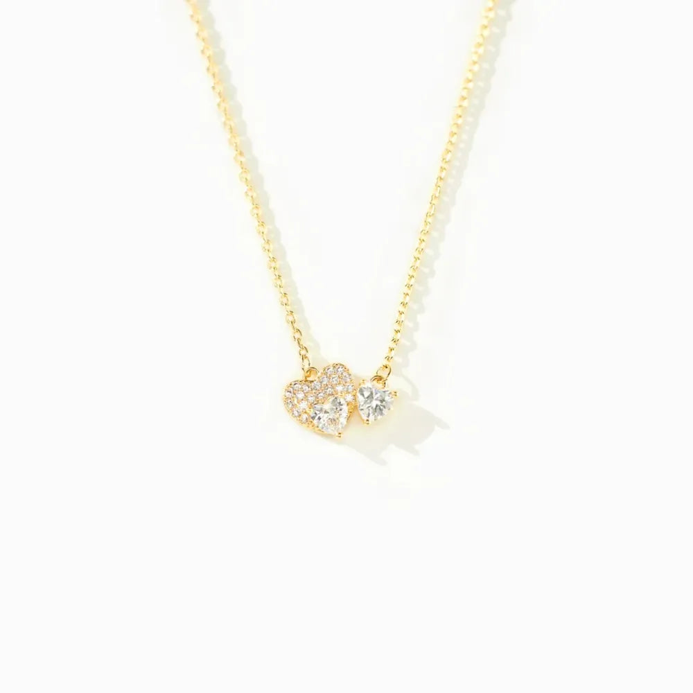 Gold necklace with two heart-shaped zirconia charms, one paved with small stones.