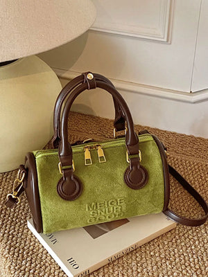 Green barrel crossbody bag with brown trim and handles, embossed text detail.