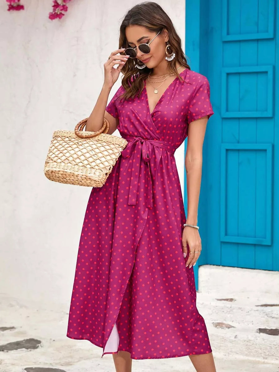 Wrap dress in magenta with red polka dots, V-neck, short sleeves, tie waist, and midi length.